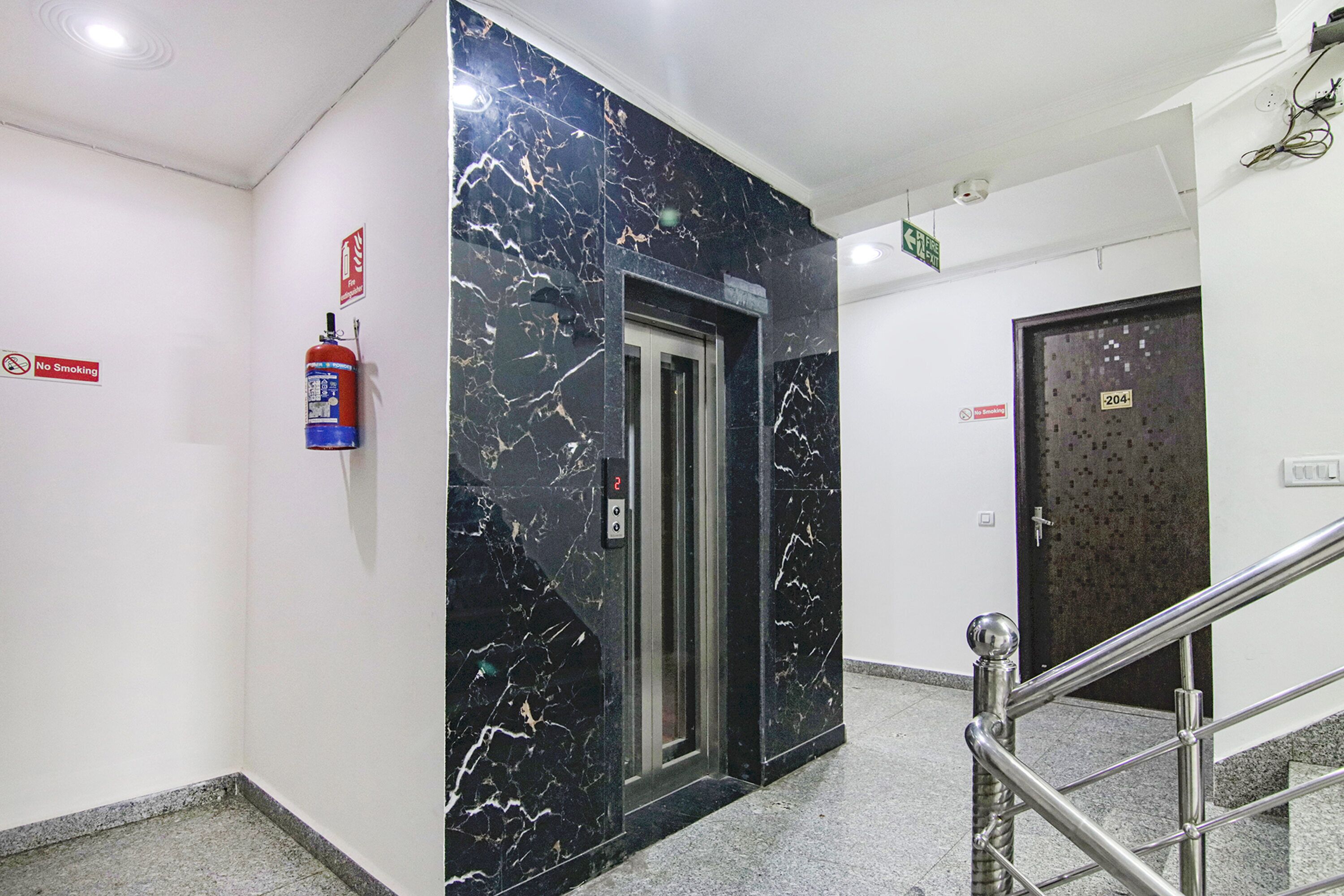 A hallway with a marble wall, a fire extinguisher, a no smoking sign, an elevator, and a door with a number sign.