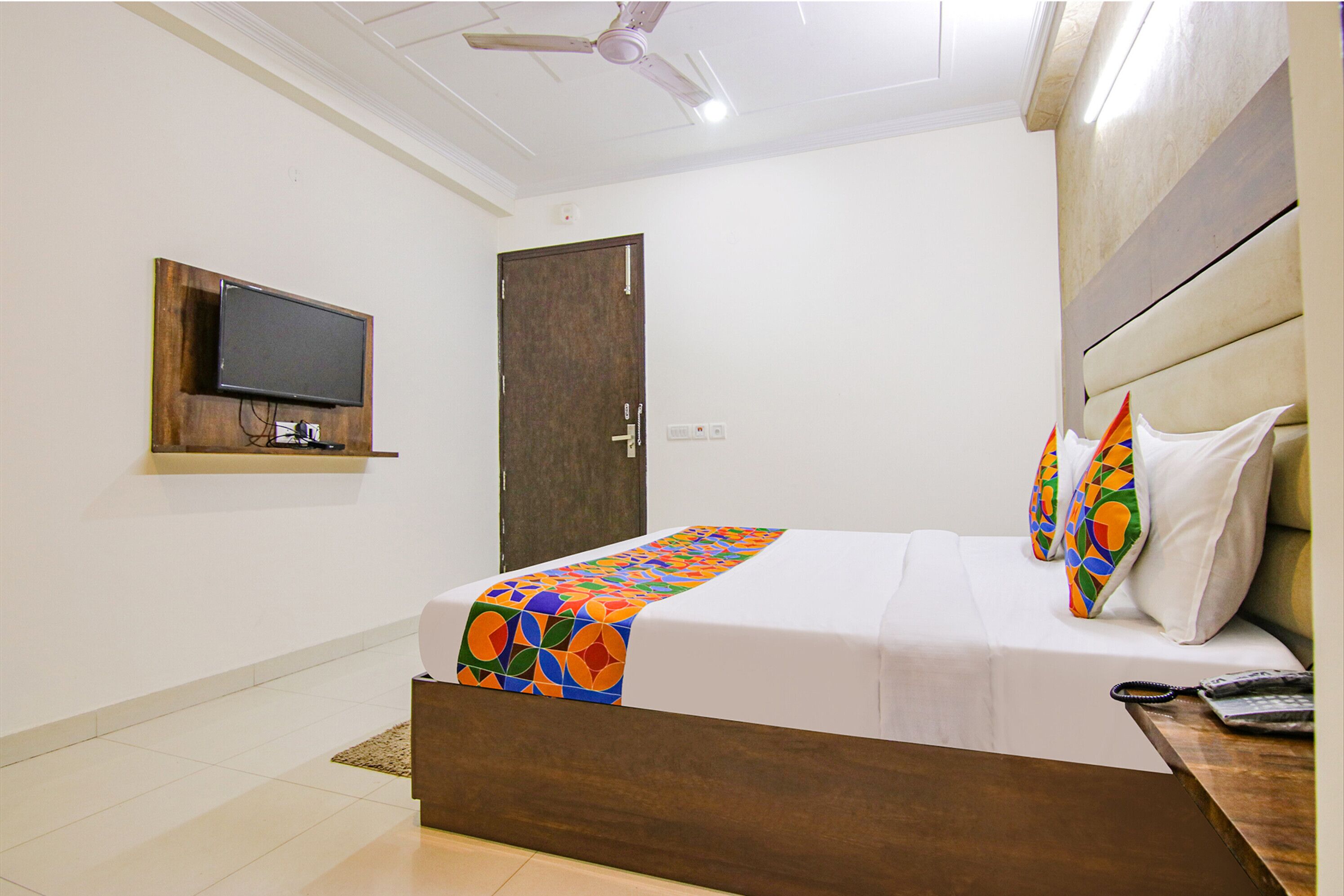 A hotel room with a bed, a television mounted on the wall, and a ceiling fan.