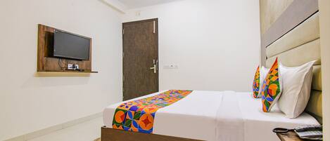 A hotel room with a bed, a television mounted on the wall, and a ceiling fan.