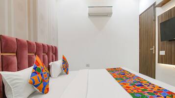 A hotel room with a bed, a red upholstered headboard, a white wall, and a mounted television.