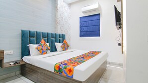 A modern hotel room with a large bed, a blue headboard, and a flat-screen TV mounted on the wall. - Fabhotel Yellow Leaf (Ludhiana)