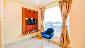 A room with a large window, a blue chair, a mounted TV, and a shelf with items. - Fabhotel Aqua Tulip (Kolkata)