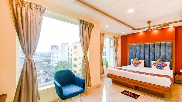 A hotel room with a large bed, a blue chair, a ceiling fan, and a view of the city through the window. - Fabhotel Aqua Tulip (Kolkata)