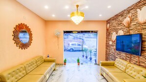 A reception area with two sofas, a chandelier, a TV, and a stone wall with floral decorations. - Fabhotel Aqua Tulip (Kolkata)
