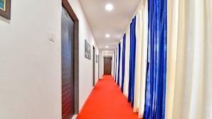 A hallway with a red carpet, blue and white curtains, and a door with a geometric pattern. - Fabhotel Infinity (Vadodara)