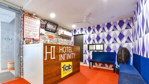 A reception area with a wooden reception desk, a sign for Hotel Infinity, and a blue seating area. - Fabhotel Infinity (Vadodara)