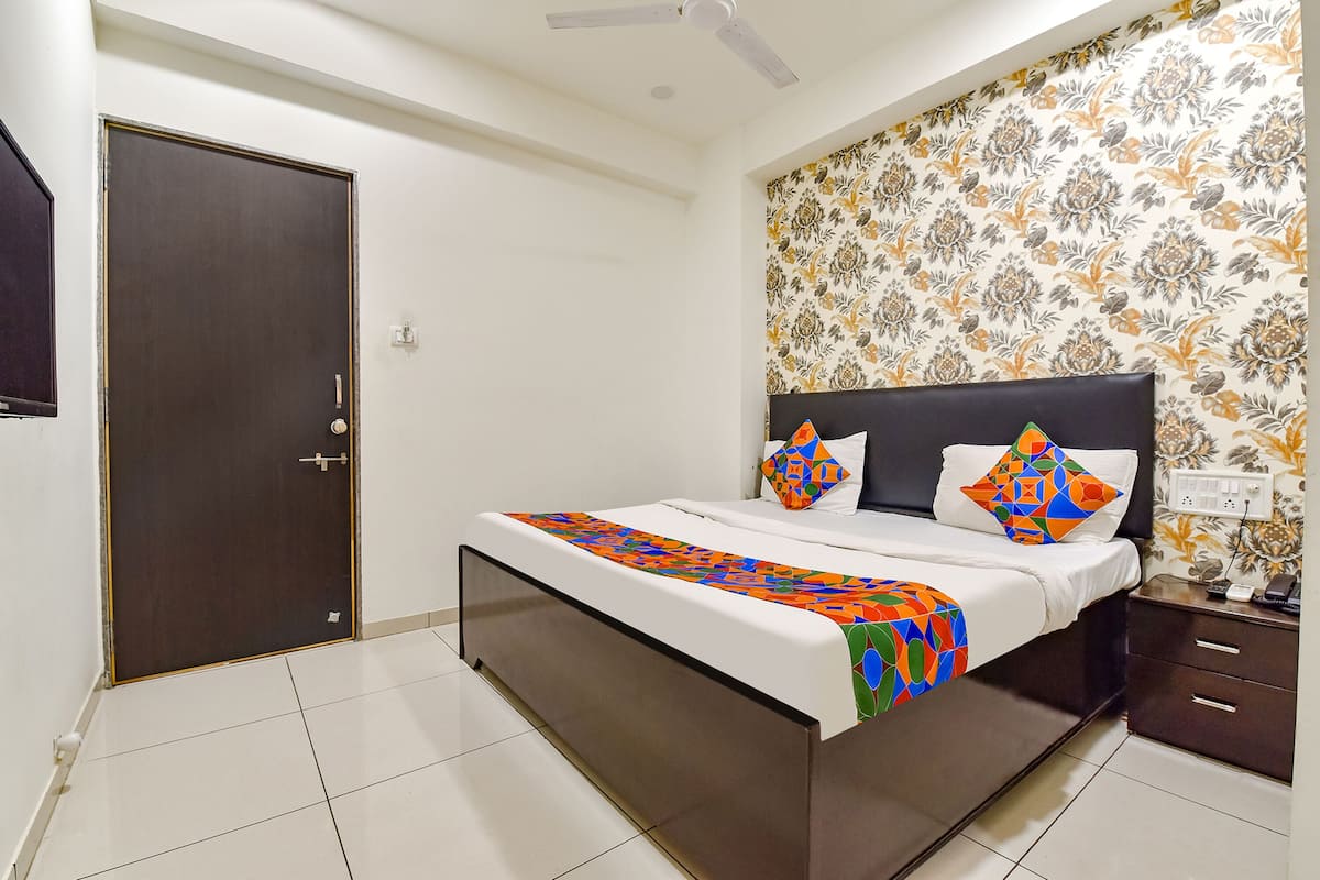 A bedroom with a bed, a nightstand, a wall-mounted TV, and a door.