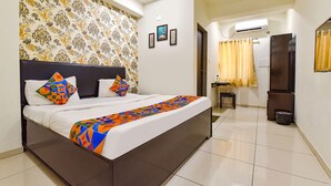 A neatly arranged bedroom with a large bed, a small table, and a mirror. - Fabhotel Infinity (Vadodara)