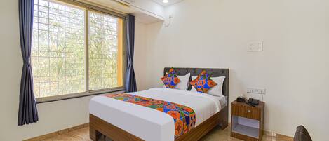 A bedroom with a bed, a nightstand, and a window with curtains.