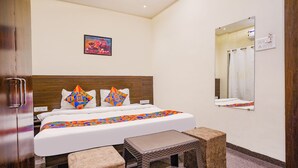 A hotel room with a wooden headboard, a bed with colorful geometric pillows, a small table, and a mirror on the wall. - Fabhotel Desire (Indore)