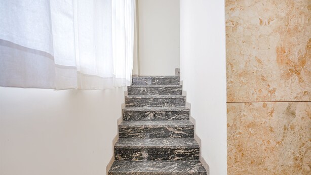 A staircase with dark marble steps leading upwards, flanked by white walls and a beige textured wall on the right. - Fabhotel Desire (Indore)