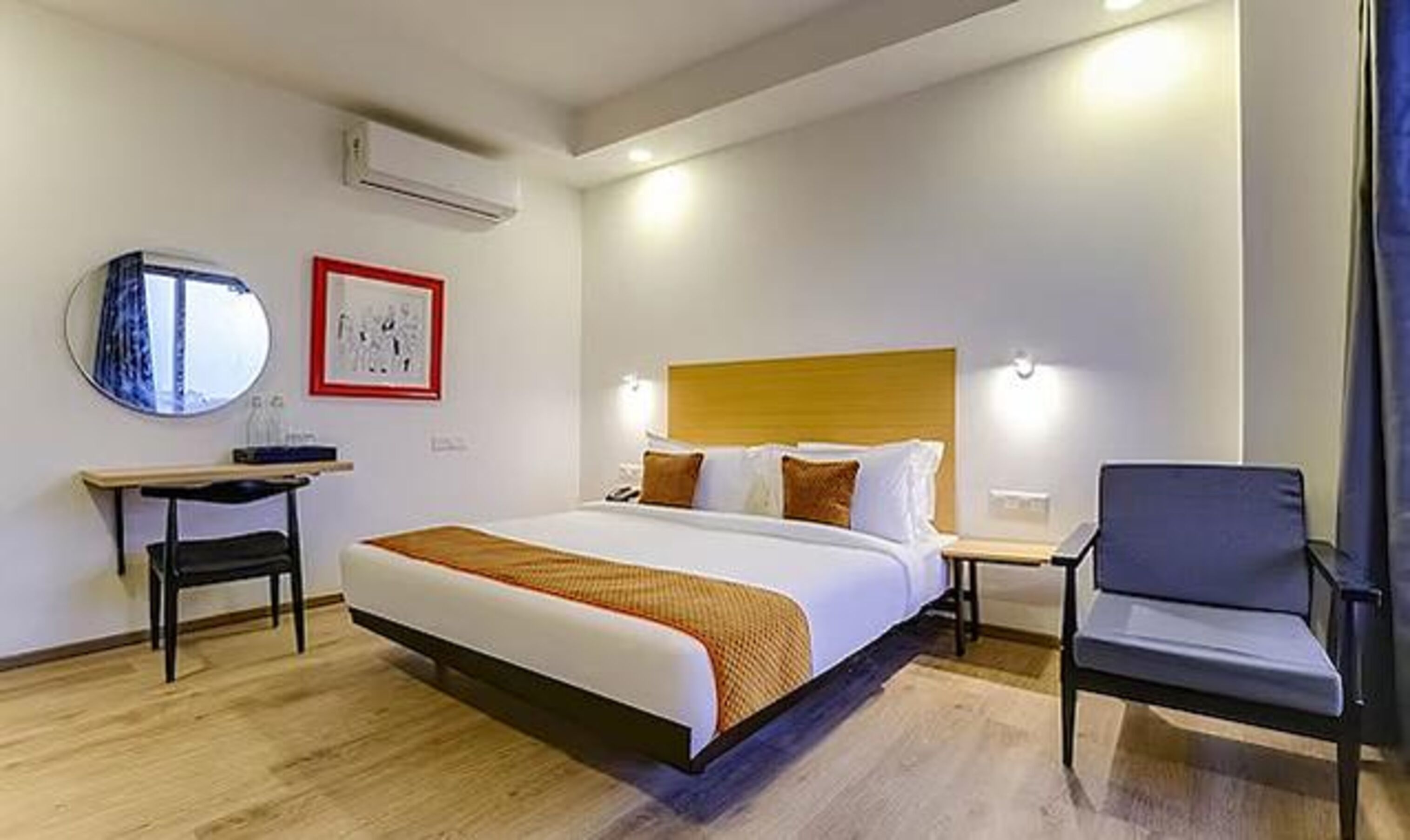 A hotel room with a large bed, bedside tables, a chair, a mirror, and artwork on the wall.