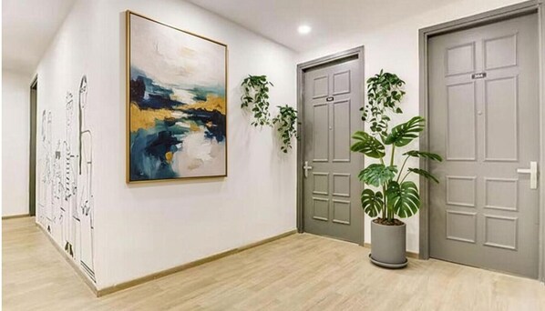 A hallway with two doors, a large abstract painting, and a potted plant.
