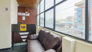 A hotel reception area with a leather chair, a reception desk with a 'fab hotels' sign, and a view of the city through large windows. - Via Athidhi Stay Inn (Hyderabad)