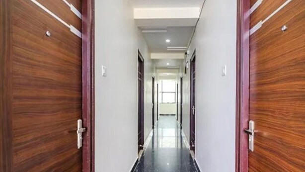 A corridor with wooden doors, white walls, and a shiny black floor. - Via Athidhi Stay Inn (Hyderabad)