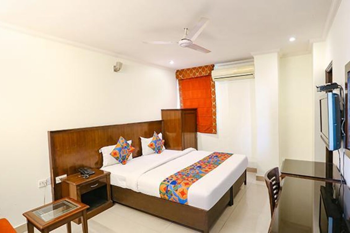 A hotel room with a wooden bed, a nightstand, a desk, and a television.