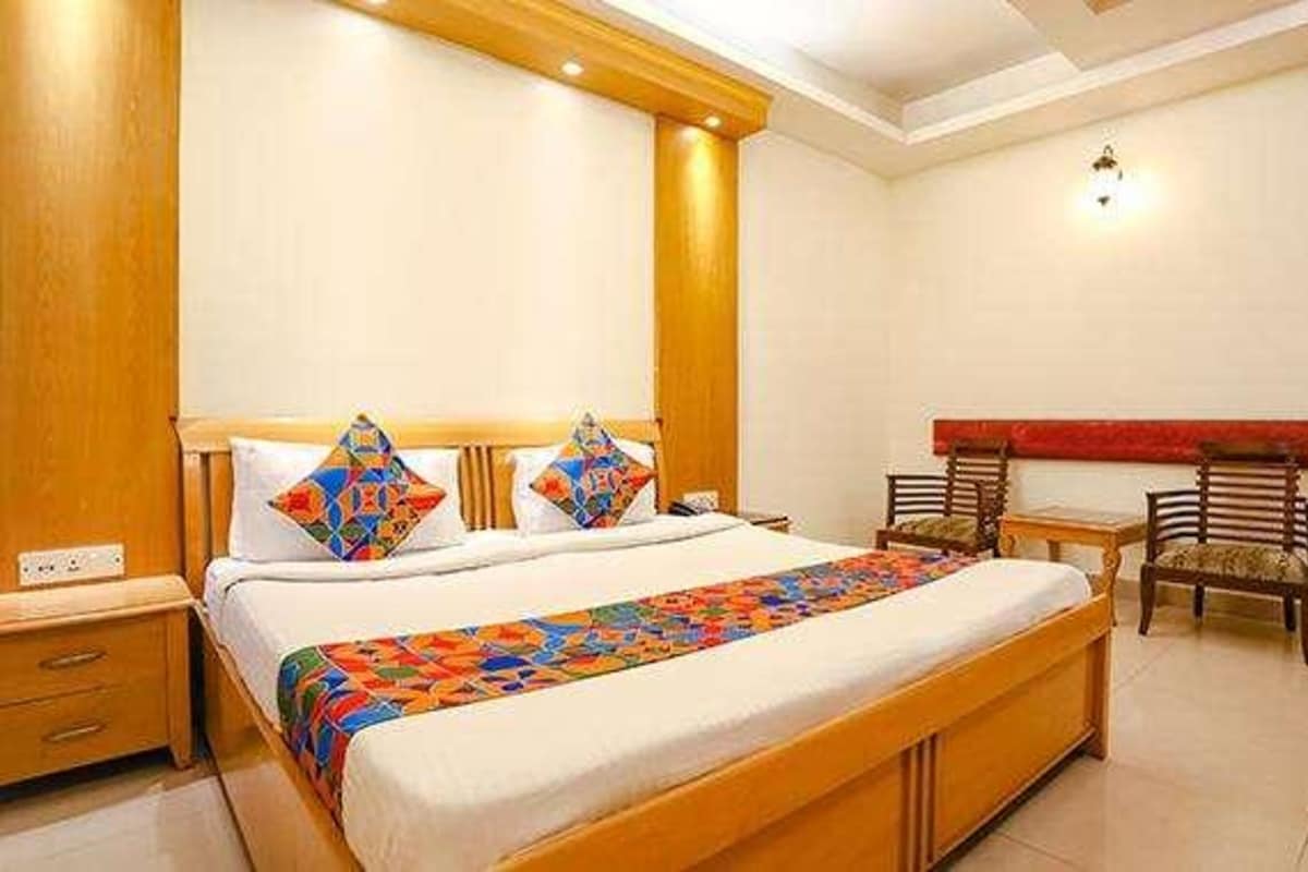 A hotel room with a large bed, wooden headboard, two bedside tables, and a red accent wall.