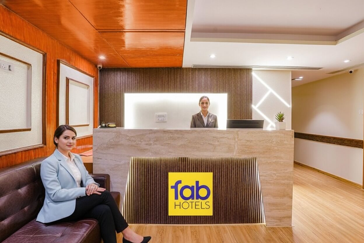Ein Empfangsschalter mit dem Logo 'fab hotels', eine Rezeptionistin und ein Gast, der auf einer Couch sitzt.