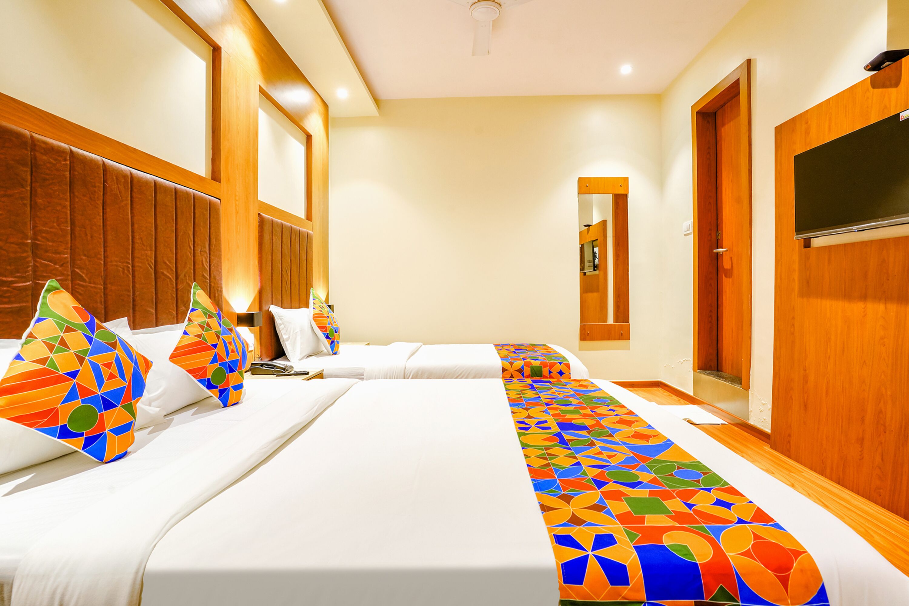 A hotel room with two beds, a wooden headboard, a large mirror, and a television.