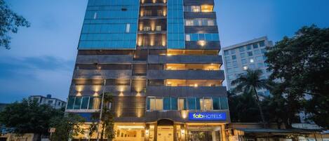 A multi-story hotel with a modern glass facade, a prominent 'fab hotels' sign, and a well-lit entrance with steps leading up to the door.