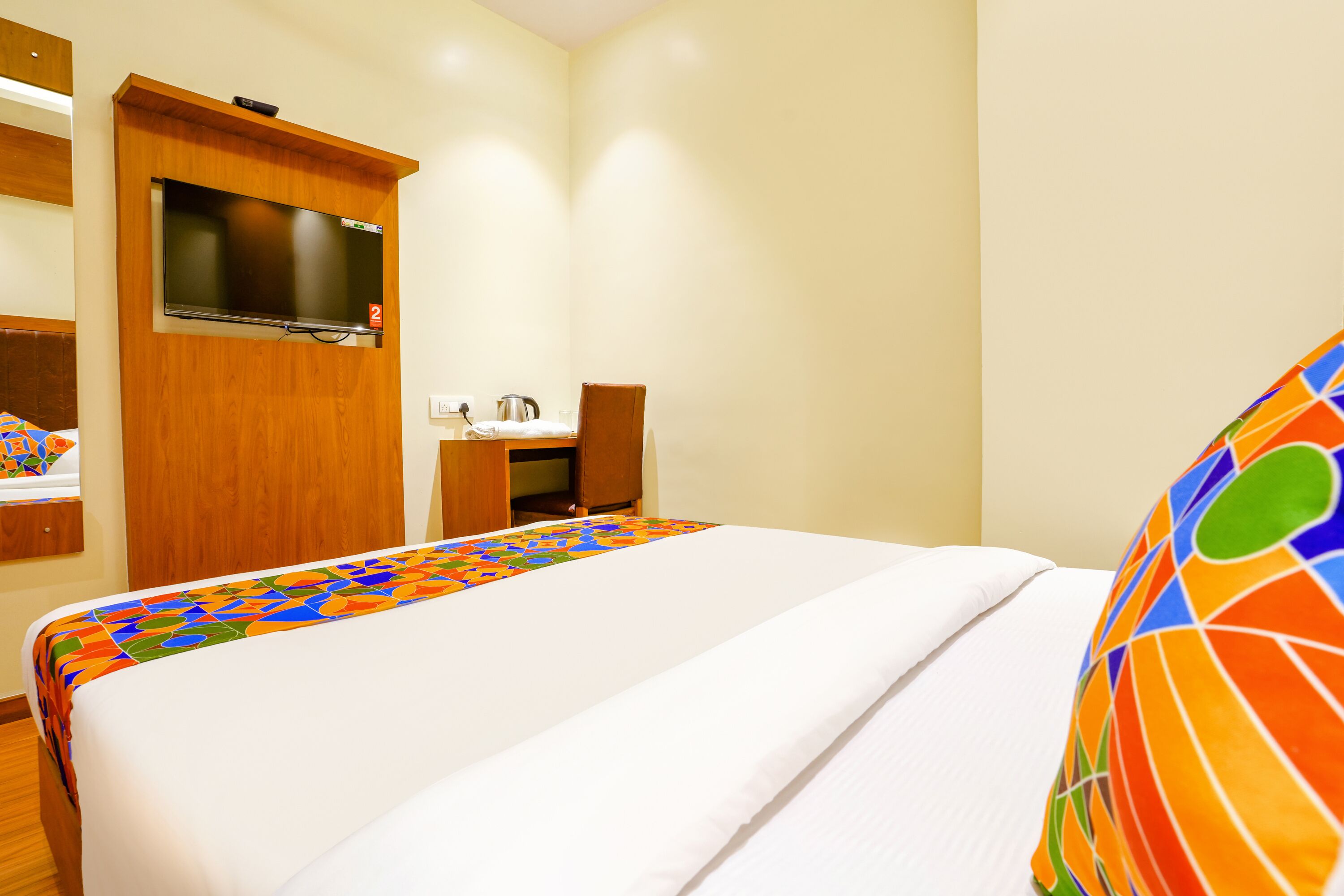 A hotel room with a bed, a TV mounted on the wall, a desk with a chair, and a bathroom area.
