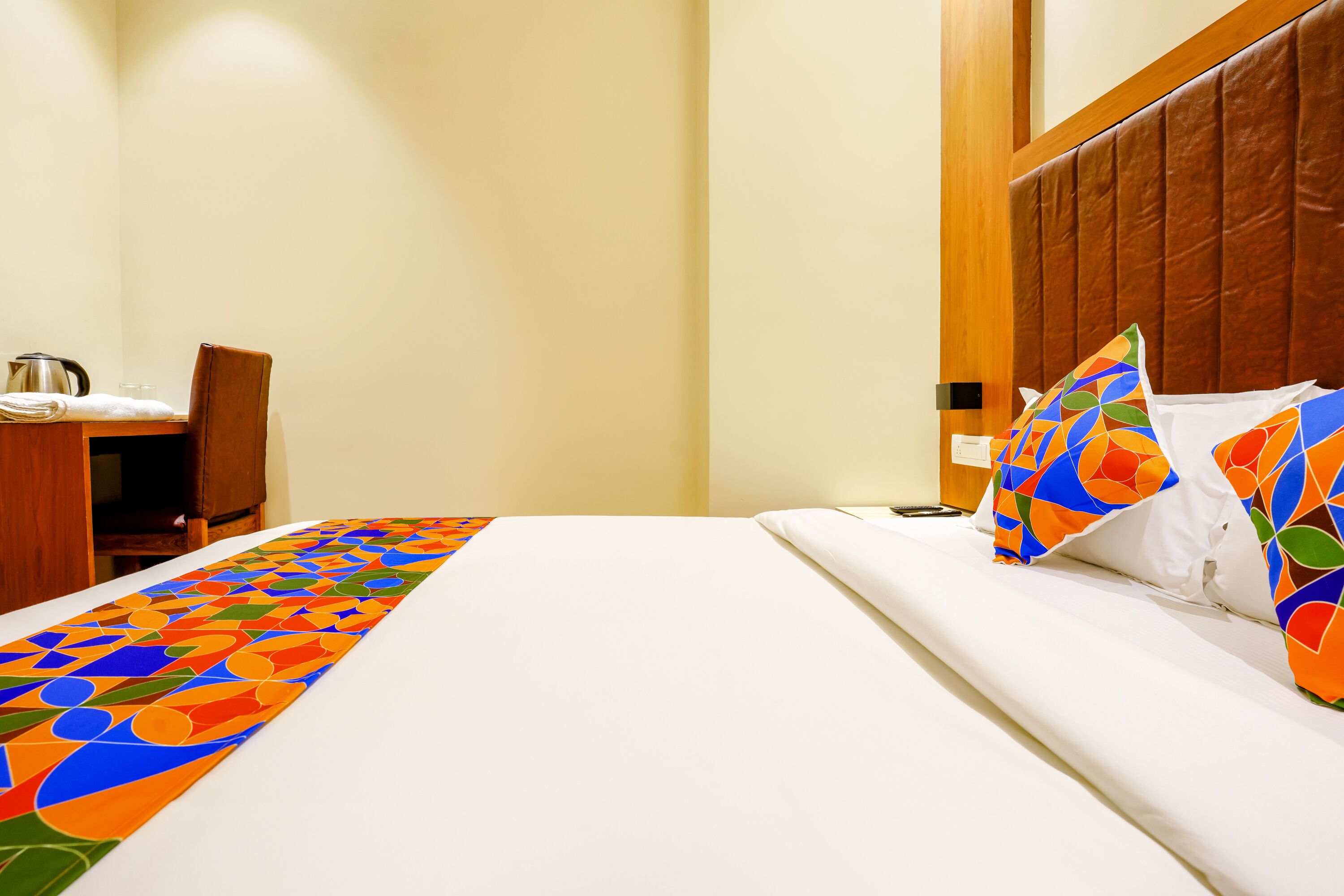 A hotel room with a neatly made bed, a wooden headboard, and a desk with a chair.