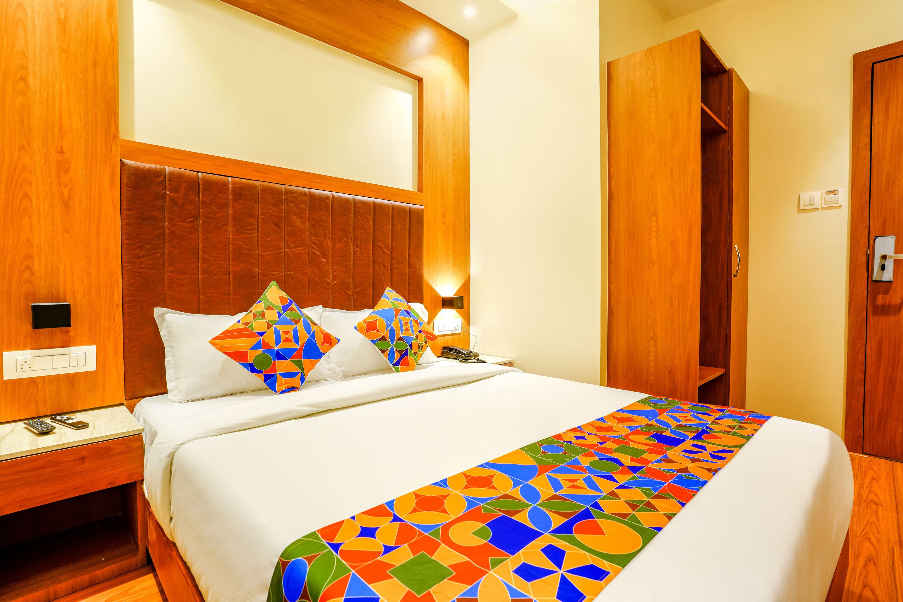 Een hotelkamer met een groot bed, een houten hoofdeinde en een kleurrijk bedspread met een geometrisch patroon.
