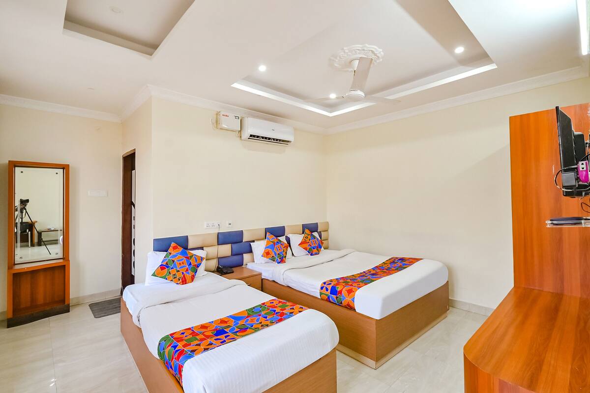 A hotel room with two beds, a wooden desk, a mirror, and an air conditioning unit.