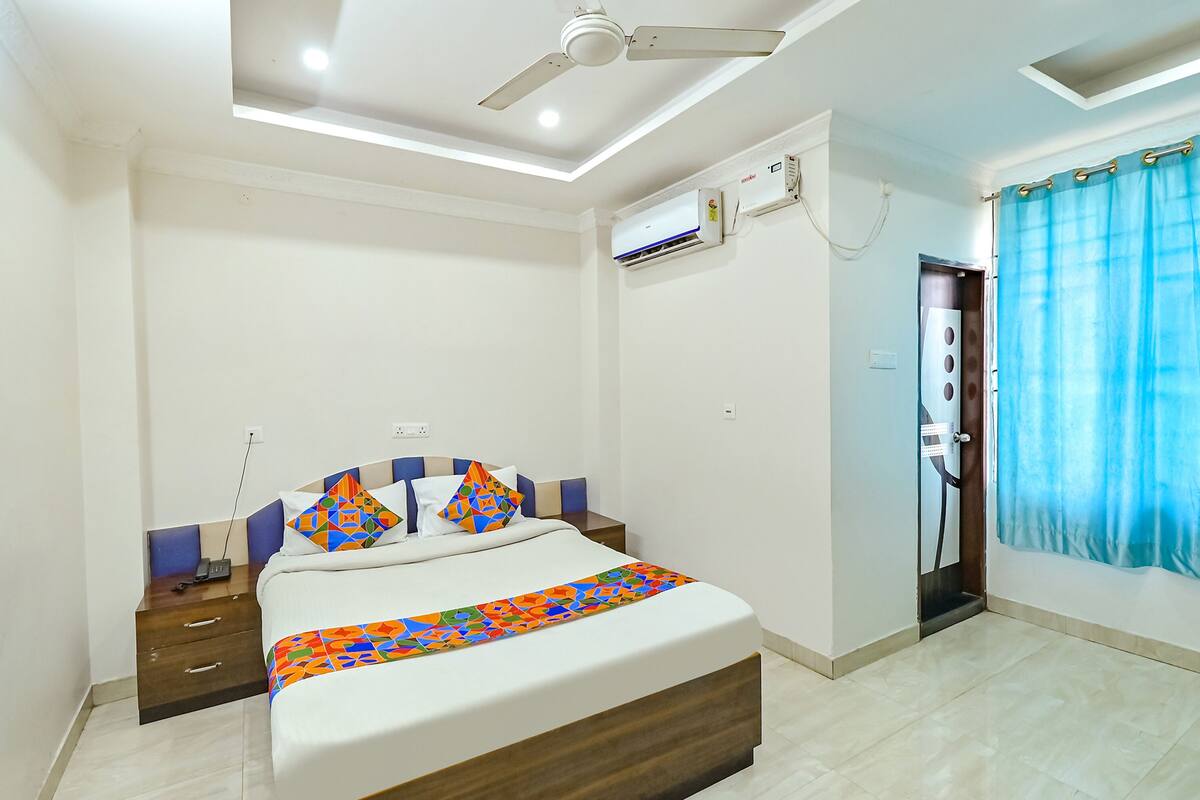A bedroom with a bed, bedside tables, an air conditioning unit, a ceiling fan, and a window with curtains.