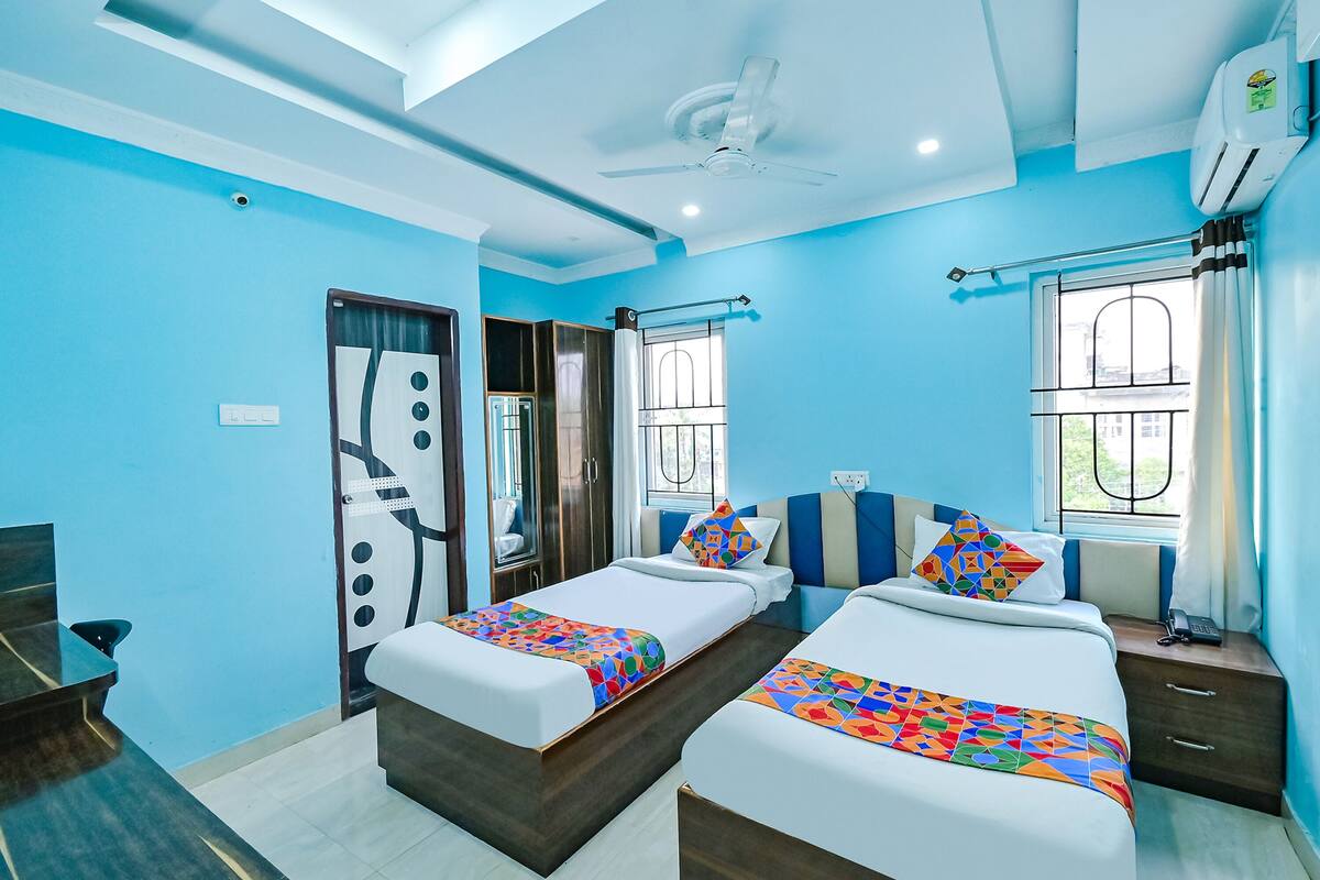 A hotel room with two beds, a ceiling fan, an air conditioning unit, and a window with curtains.