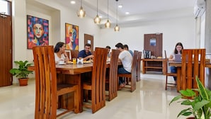 Un comedor con mesas y sillas de madera, ventiladores de techo y plantas en macetas.