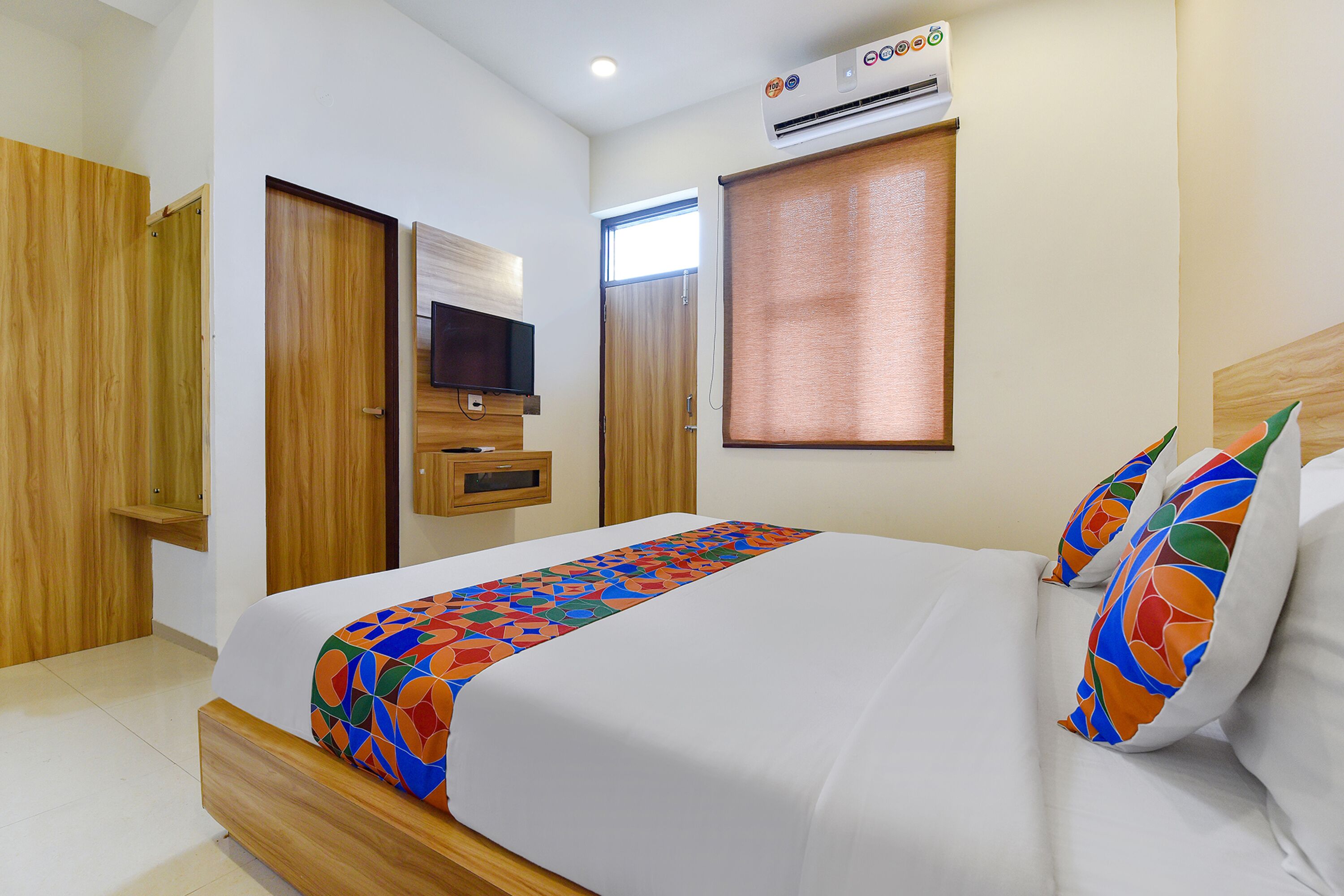 Una habitación de hotel con cama, televisor, ventana con persianas y unidad de aire acondicionado.