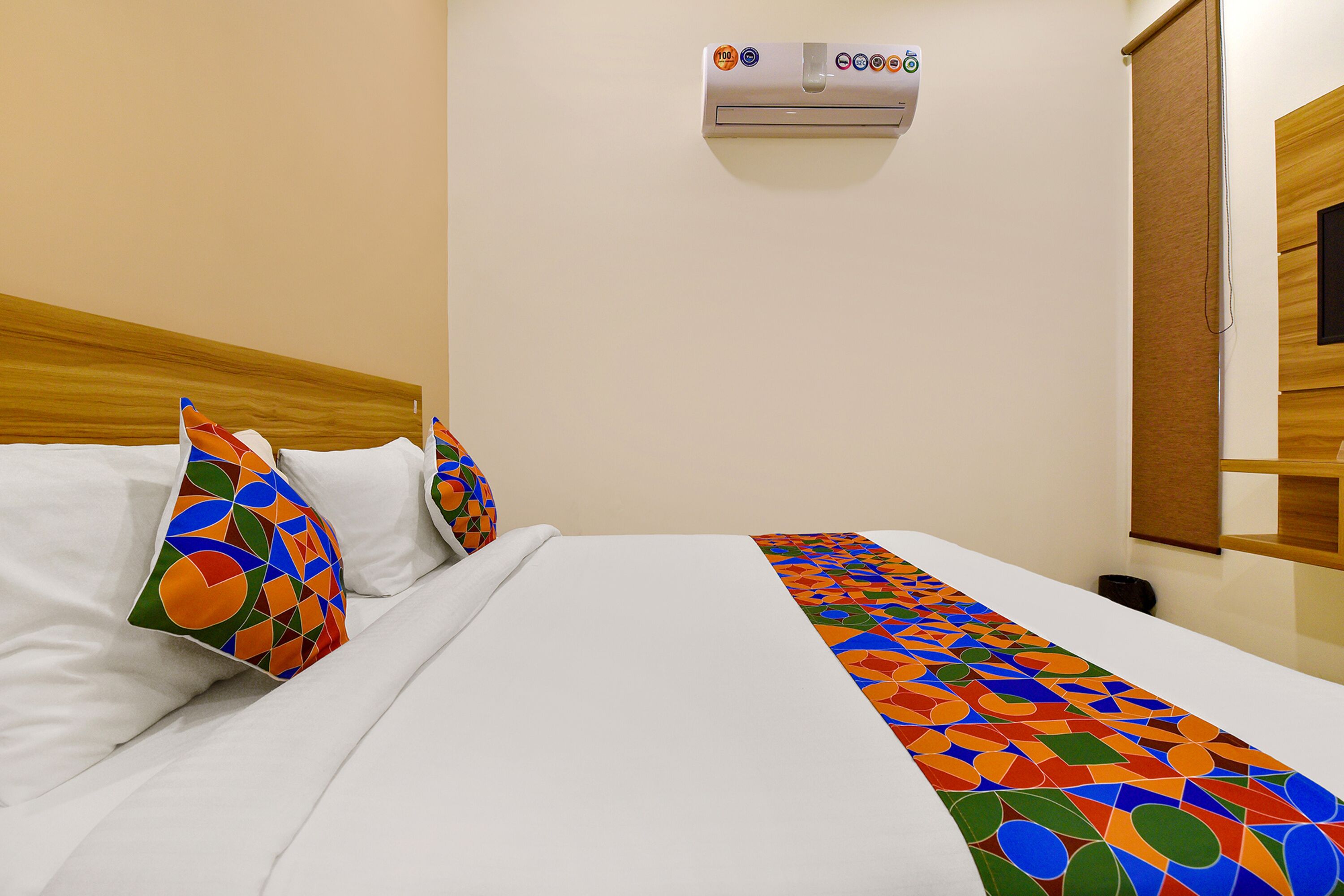 A hotel room with a bed, pillows, a blanket, an air conditioning unit, and a wooden door.