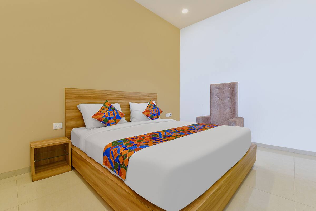 A modern bedroom with a wooden bed frame, white bedding, and colorful geometric pillows.