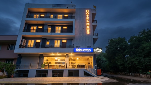 Un hotel de varios pisos con un letrero llamativo que dice 'HOTEL OXIS', un letrero que dice 'fabHOTELS' y un reflejo en una fuente frente a él.