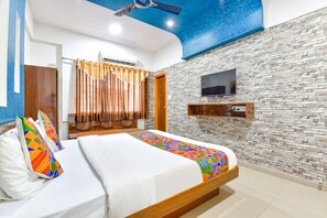 A hotel room with a bed, a TV mounted on the wall, and a ceiling fan. - Fabhotel Raj Ratna (Ahmedabad)