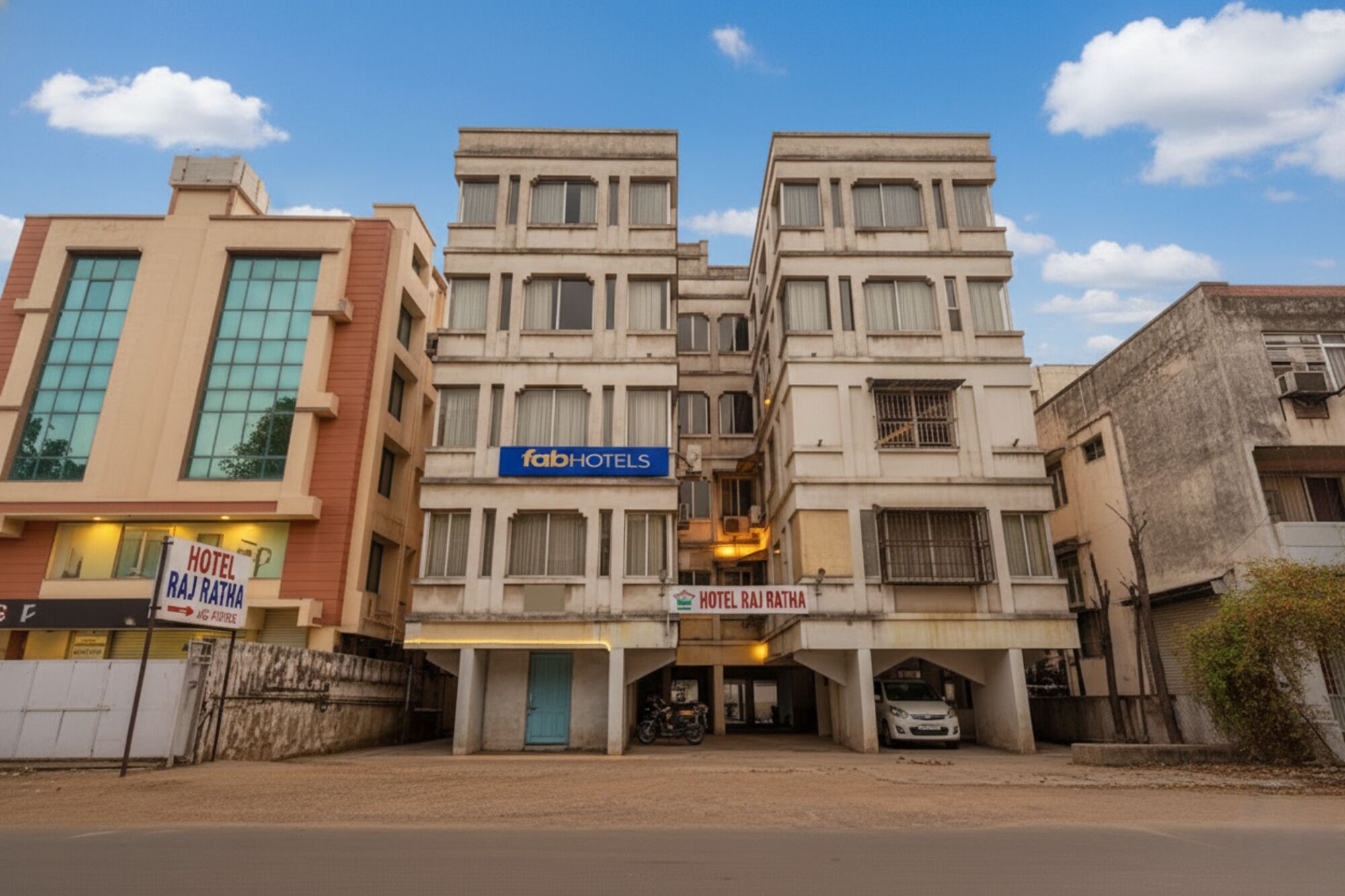 Een meerlaags gebouw met een bord waarop 'fabHOTELS' en 'HOTEL RAJ RATHA' staan, wat een hotelcomplex aangeeft.