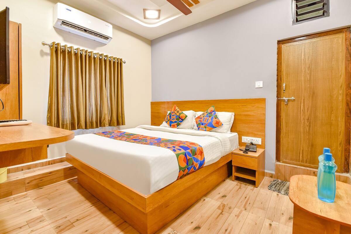 Ein aufgeräumtes Hotelzimmer mit einem hölzernen Bett, einem Nachttisch, einem Schreibtisch und einer Klimaanlage.