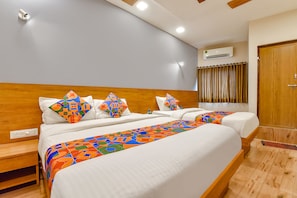 A hotel room with two beds, a wooden headboard, a colorful bed runner, and an air conditioning unit on the wall. - FabHotel Gokul Villa (Ahmedabad)