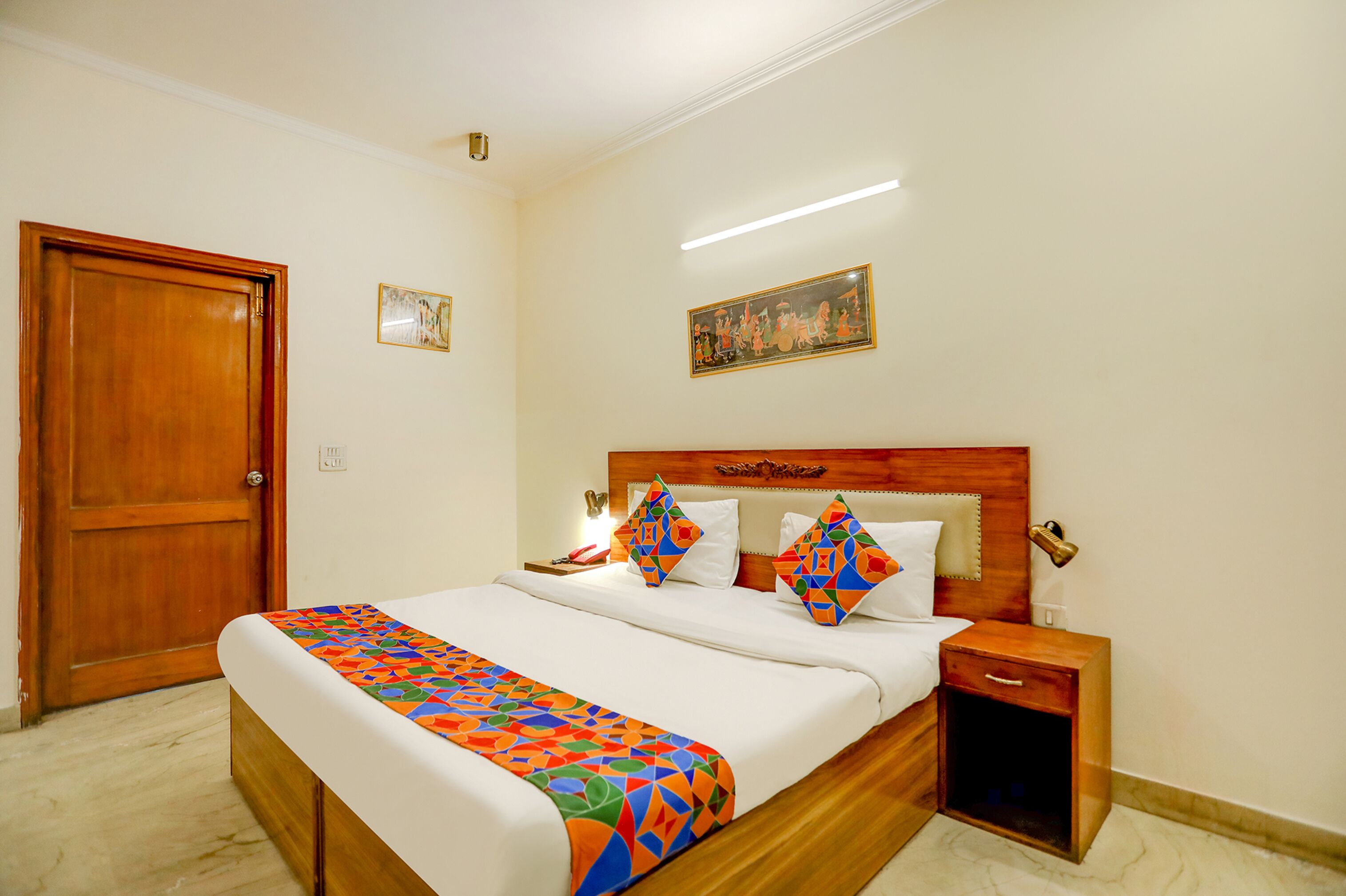 Una habitación de hotel con una cama de madera, una mesita de noche, una puerta y una lámpara fijada a la pared.