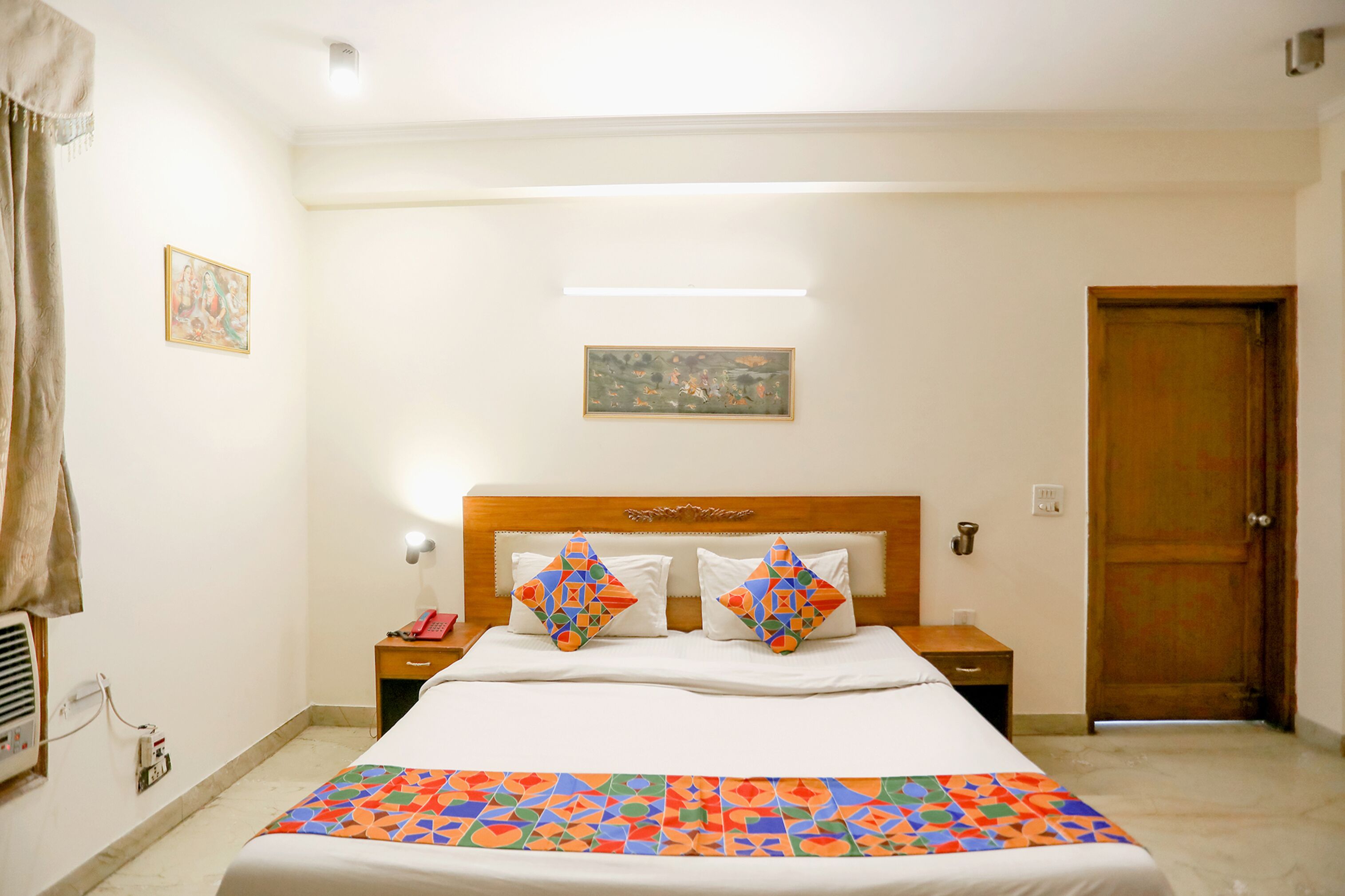 A hotel room with a bed, two nightstands, a wooden door, and a painting on the wall.