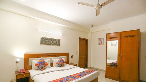 Una habitación de hotel con una cama, un armario, una mesita de noche y un ventilador de techo.