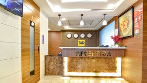 Een hotel receptie met een receptiebalie, meerdere klokken en een groot ingelijst portret aan de muur.