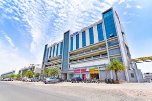 A multi-story hotel with a modern design, featuring a prominent entrance and a parking area with several cars and motorcycles.
