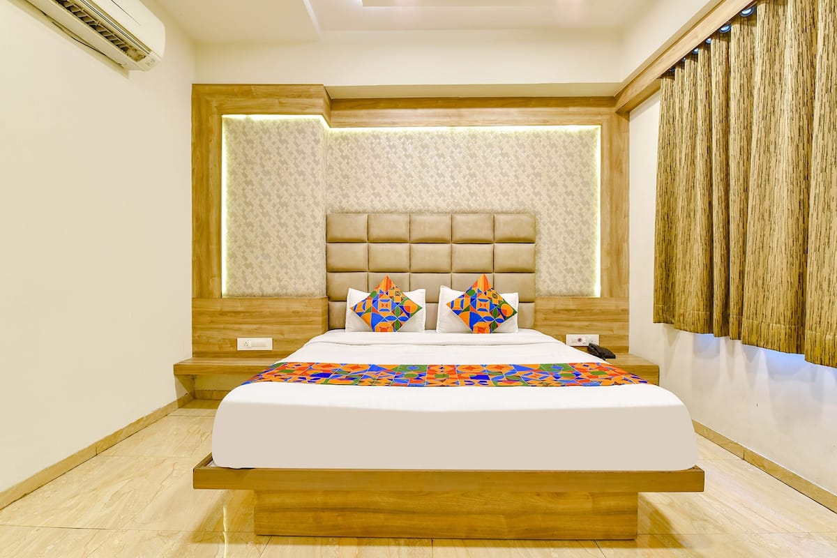 Une chambre d’hôtel moderne avec un grand lit, une tête de lit dotée d’un éclairage intégré, une table de chevet en bois et un mur décoré d’un motif.