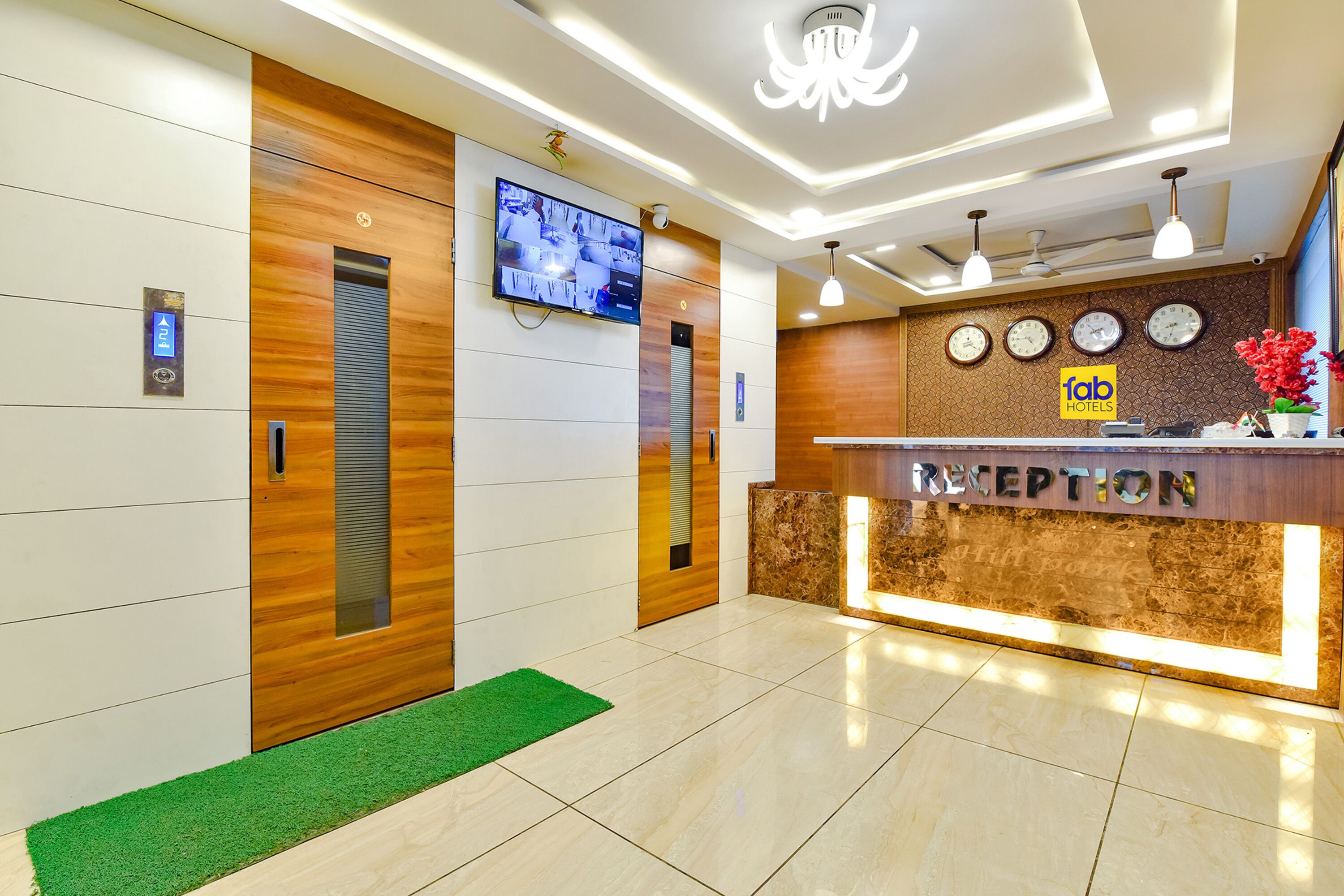 A hotel reception area with a reception desk, a digital clock, and a television mounted on the wall.