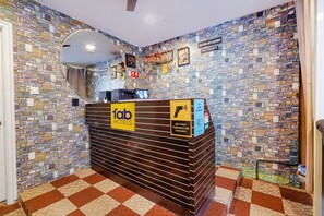 A reception desk with a 'fab hotels' sign, a mirror, a digital display, and a 'no mask' sign. - Fabexpress Kings Suites Hrbr Layout (Bengaluru)