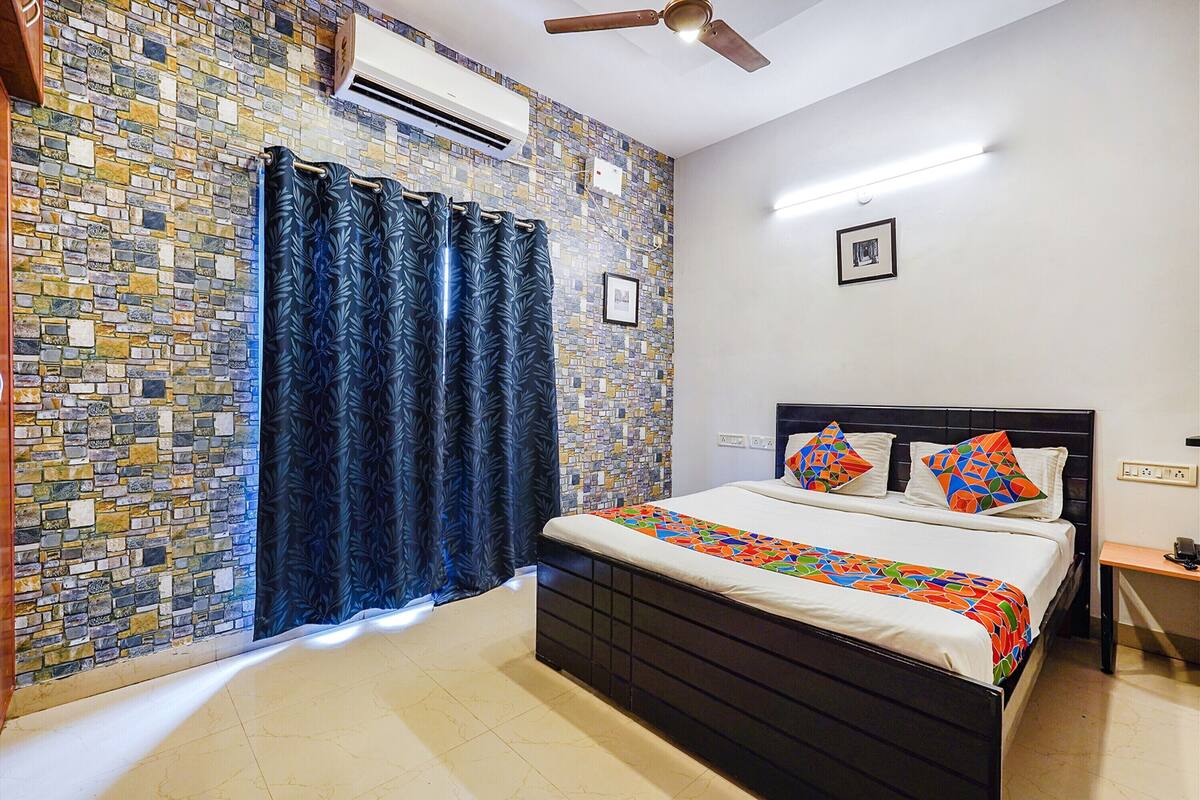 A bedroom with a patterned wall, a bed with a colorful bedspread, a ceiling fan, and a nightstand.