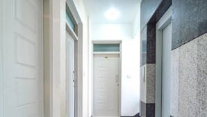 Un couloir avec des portes blanches, un sol carrelé et, au bout, une porte dont l’encadrement est de couleur verte.