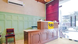 Una recepción con el rótulo 'fab hotels', una silla de madera y una ventana que da a la calle.